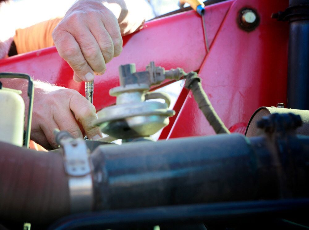 A Man Is Working on A Red Tractor with A Screwdriver — Parkes Machinery Services PTY LTD in Parkes, NSW