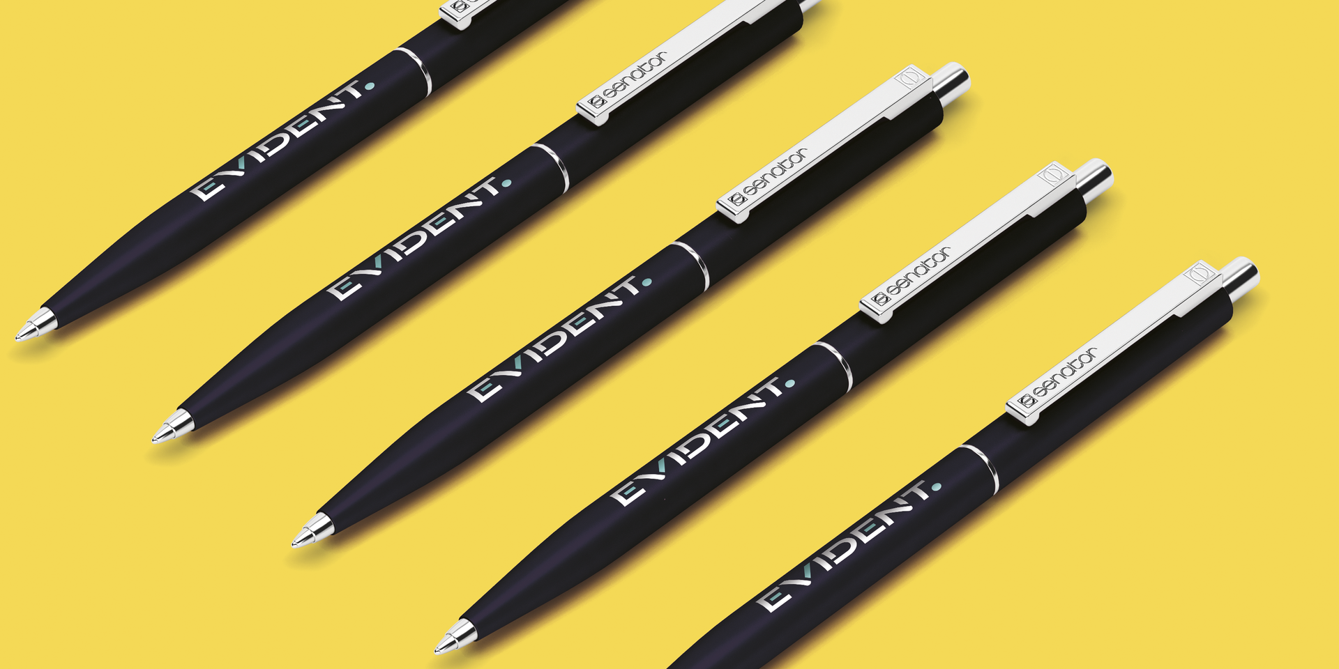 Cinq stylos noirs avec l'inscription « EVIDENT. » imprimée dessus, disposés en diagonale sur un fond jaune.