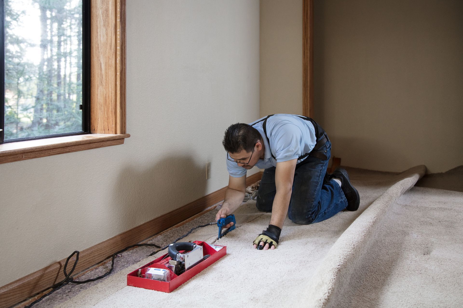 A man is kneeling down to install a carpet in a room.