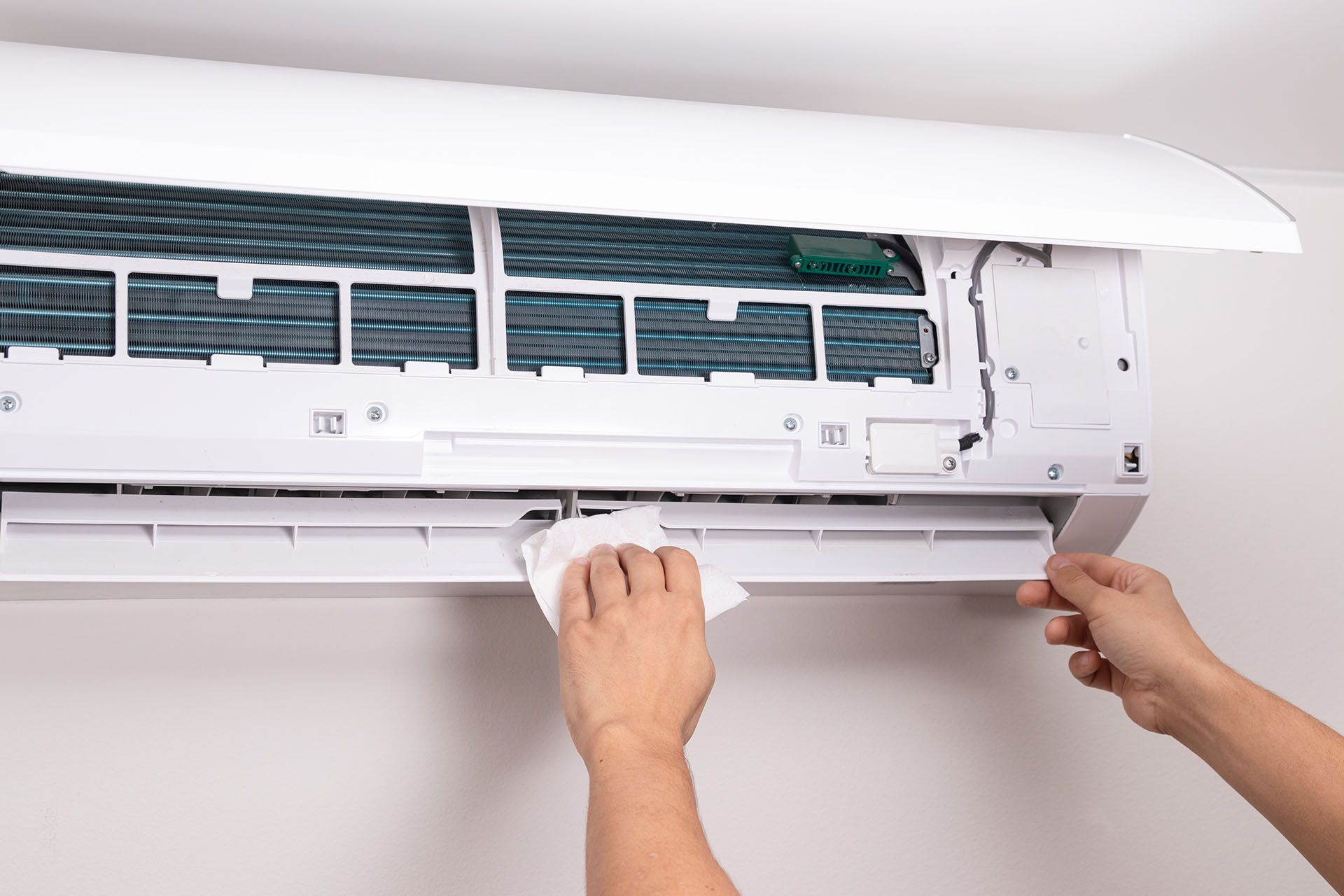 Close-up of a man cleaning the vents of an AC unit with a soft cloth.
