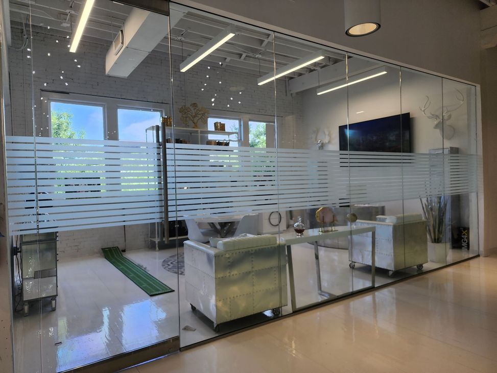 Glass-walled office reception area with modern seating, striped frosted panels, and large wall-mounted TV