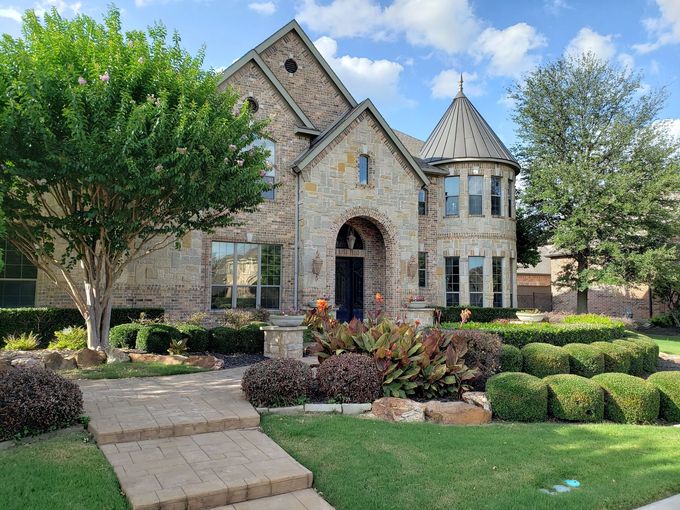 Stone house with arched entry, manicured lawn, and landscaped garden under a blue sky