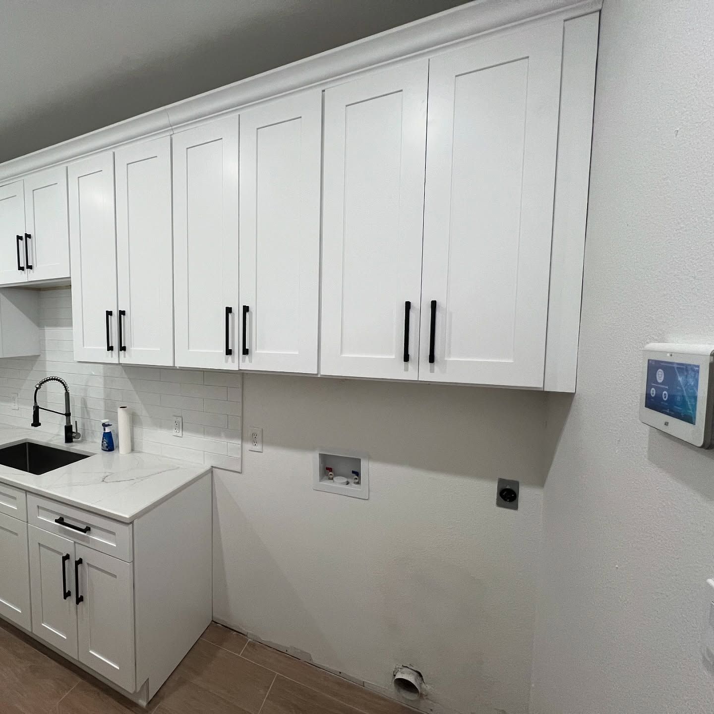 White kitchen cabinets with black handles; sink and appliance hookups visible.