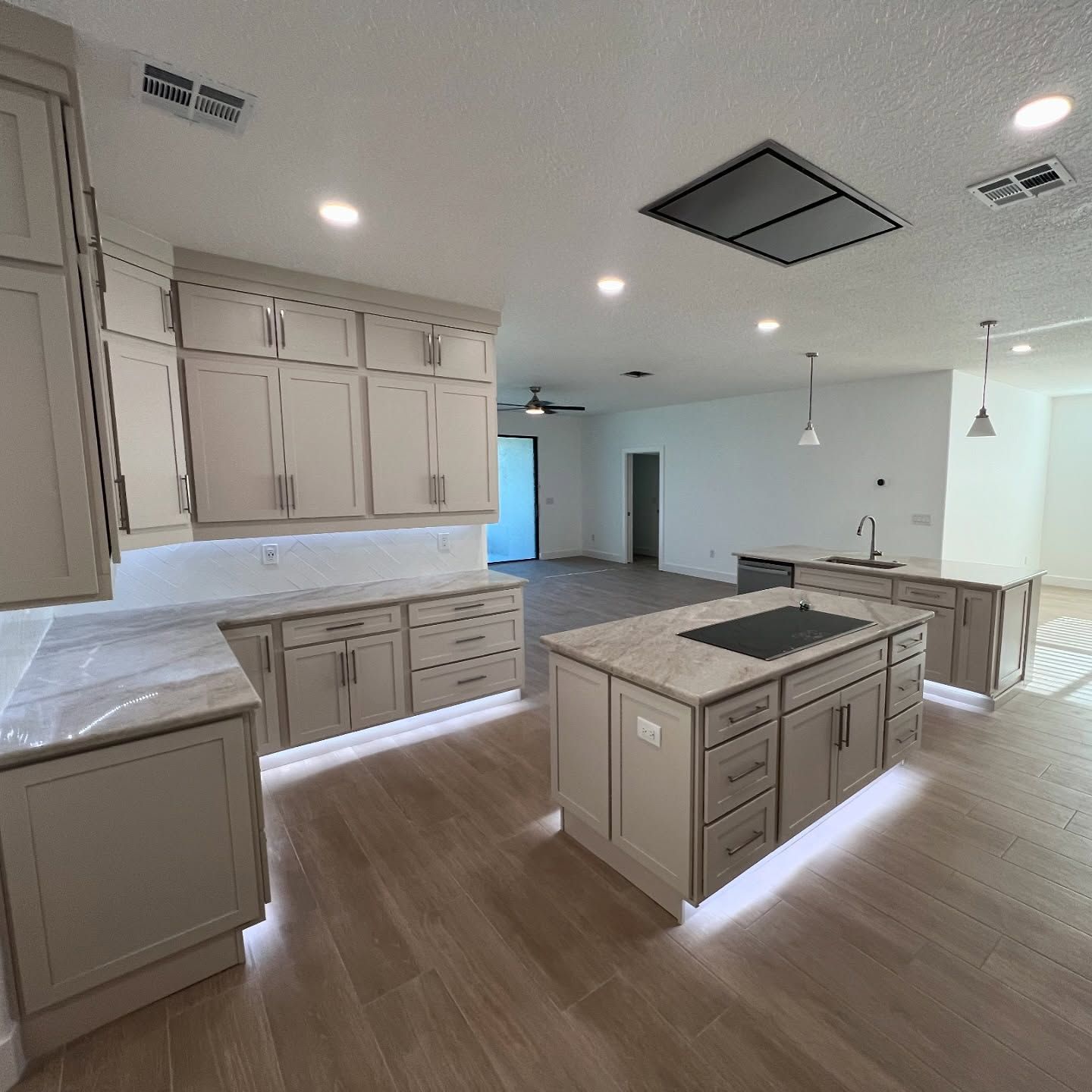 Modern kitchen with light grey cabinets, marble countertops, and island. LED lighting illuminates the cabinets and island.