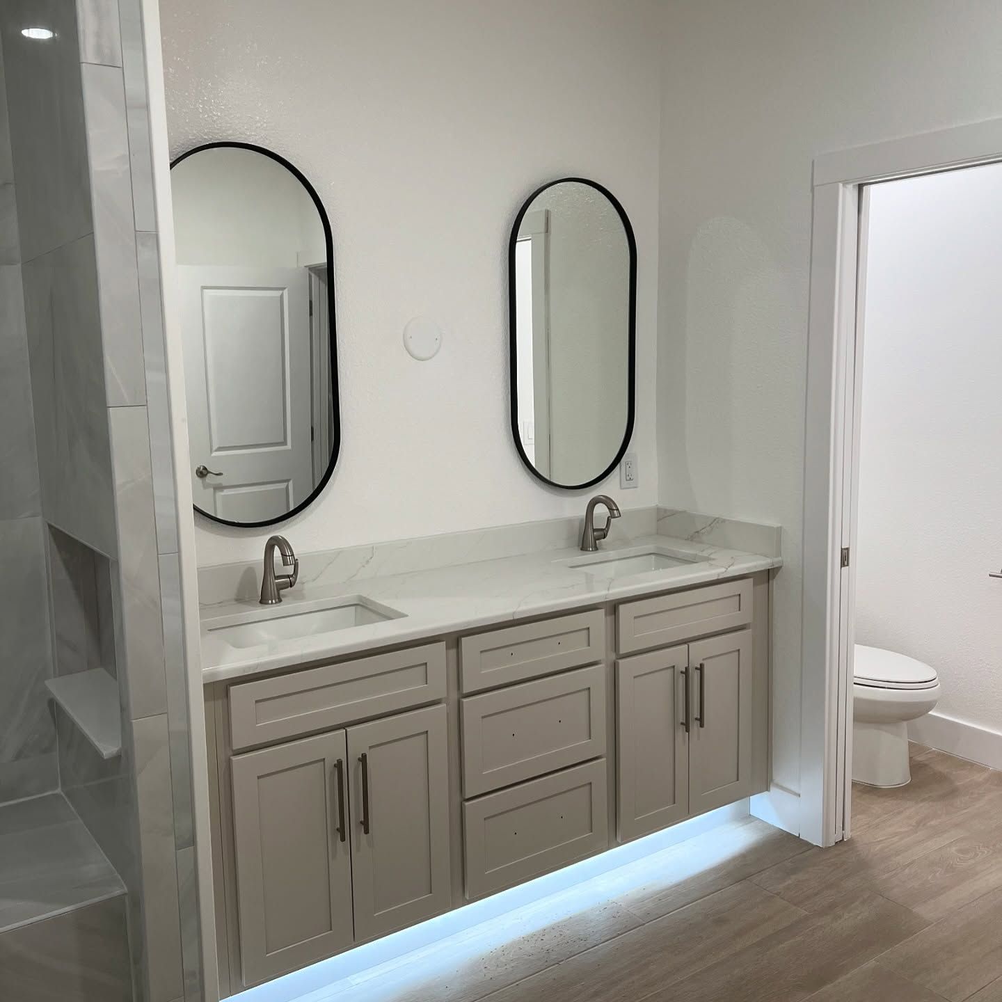 Bathroom with double vanity, oval mirrors, and under-cabinet lighting.
