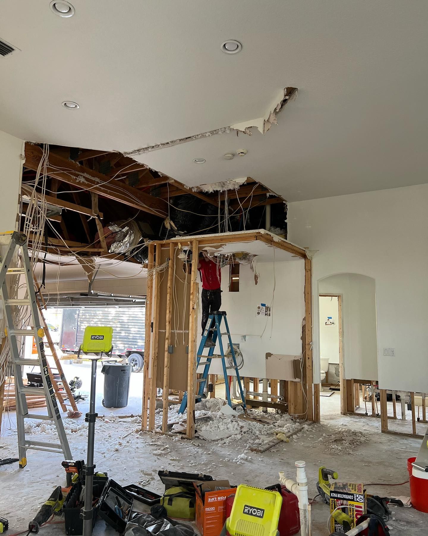 Interior under renovation: Ceiling and walls torn out. Person on ladder. Debris on floor.