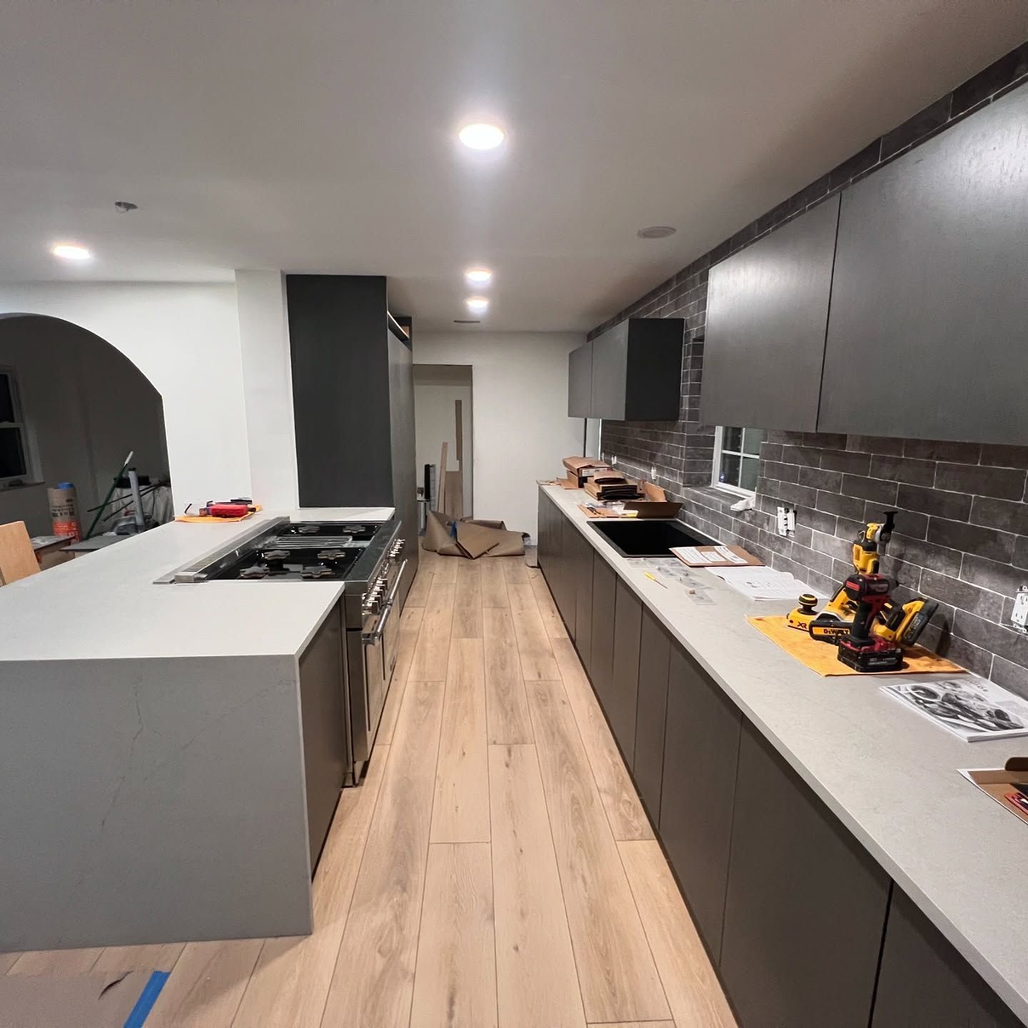 Modern kitchen with grey cabinets, light countertops, and wood flooring.