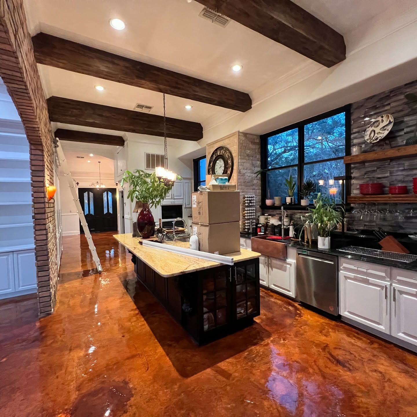 Kitchen with island, dark cabinets, wooden beams, stainless steel appliances, and brown floors.