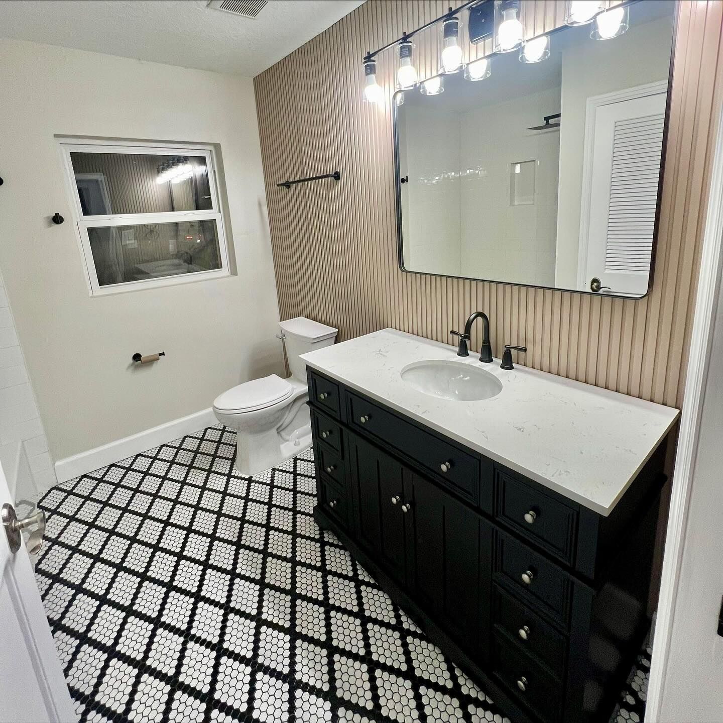 Bathroom with black vanity, patterned tile floor, and accent wall behind a mirror.