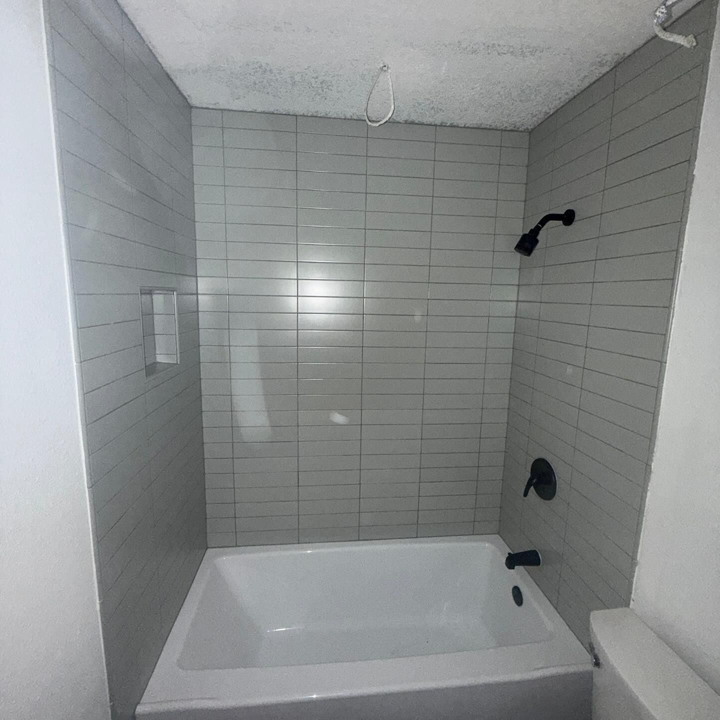 Bathroom with a white tub, gray tile walls, and black fixtures.