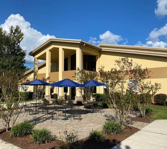 Building with patio, tables, and blue umbrellas under a sunny sky.