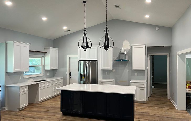 Spacious kitchen with white cabinets, blue island, stainless steel appliances, and two black pendant lights.