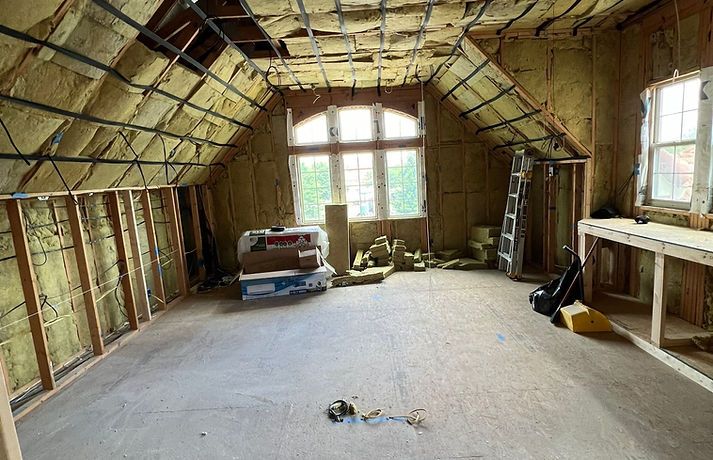 Interior of an attic under construction; exposed wood framing, insulation, and unfinished walls.