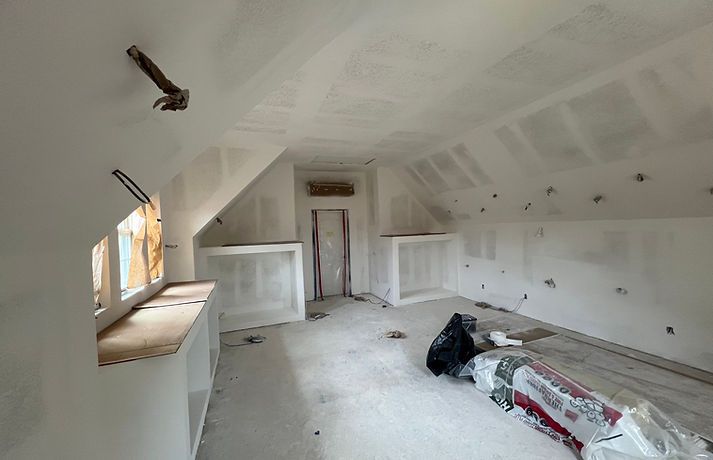 Interior of a room under construction, with drywall, exposed beams, and a window.