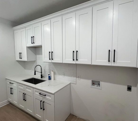 White cabinets with black hardware in a laundry room, including a sink and countertop.