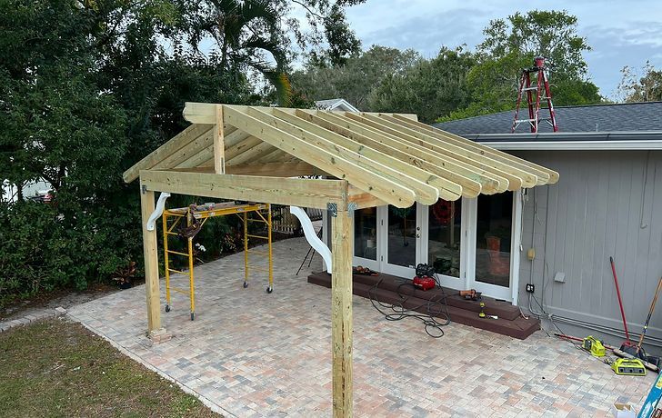 Newly built wooden pergola on a brick patio, attached to a house with glass doors.