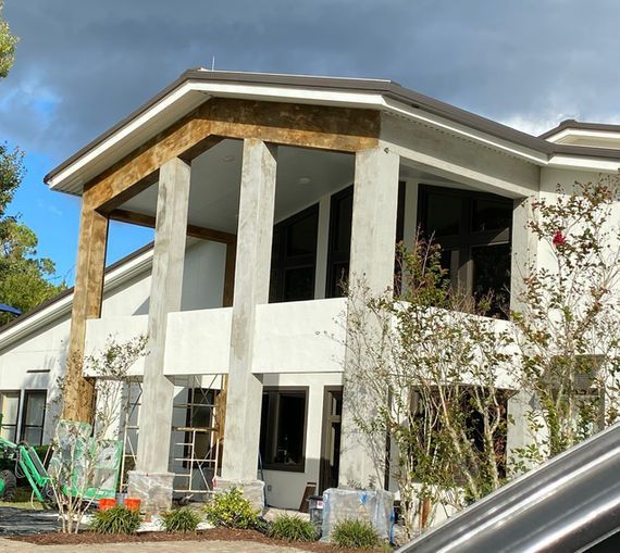 White building with brown trim and columns. Large windows, cloudy sky.
