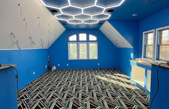 Blue room with patterned carpet and hexagonal ceiling lights. Windows and exposed wires visible.