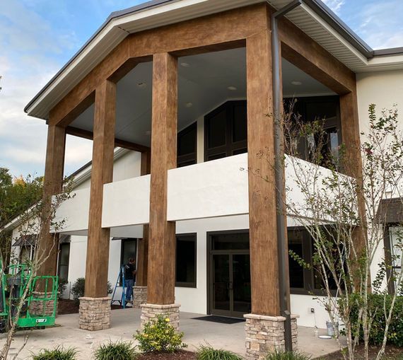 White building with brown support beams and a covered entrance. A person stands near the door.