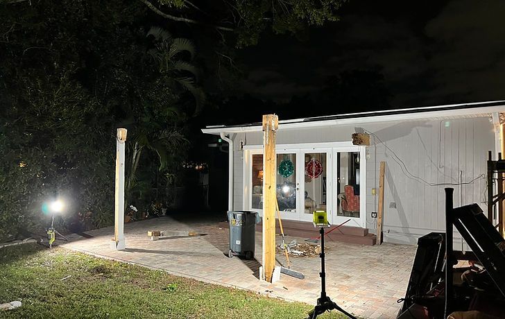 Construction site at night. Wooden posts are in front of a white building with glass doors, lights are on.