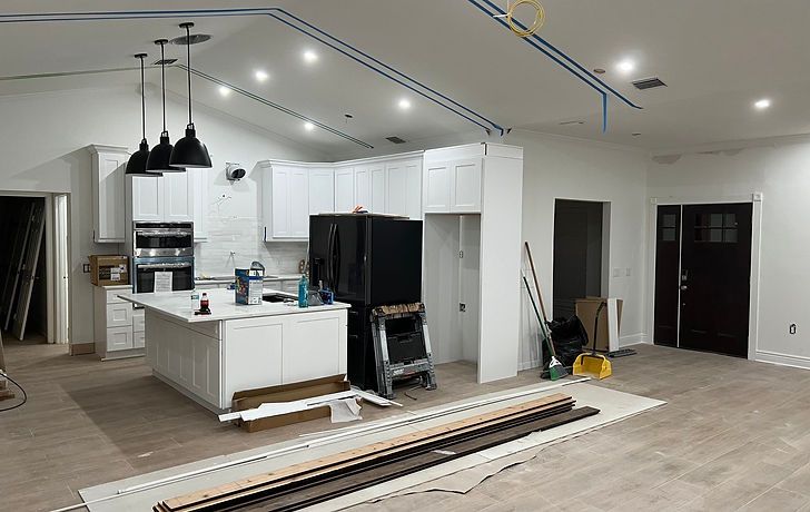Kitchen remodel in progress with white cabinets, black appliances, and pendant lights.