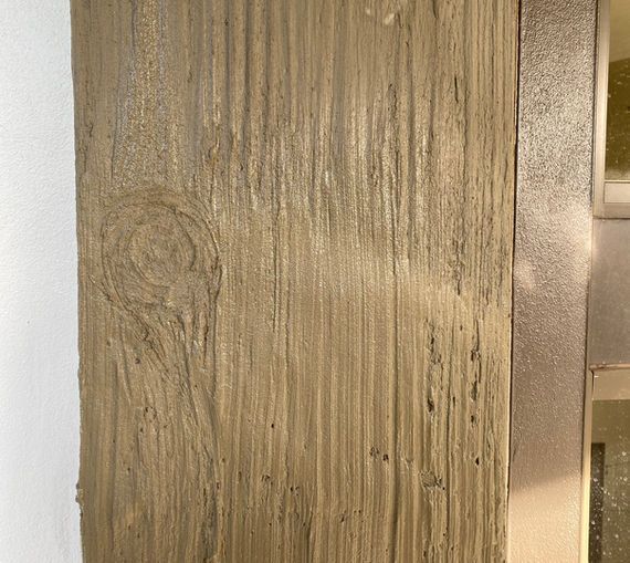 Close-up of a faux wood concrete pillar with vertical grooves and a knot. Beige and gray colors.