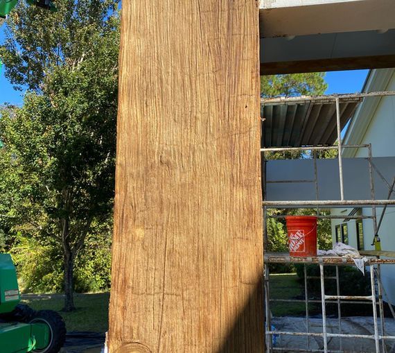 Close-up of a weathered, textured wooden column, with scaffolding and a building in the background under a blue sky.
