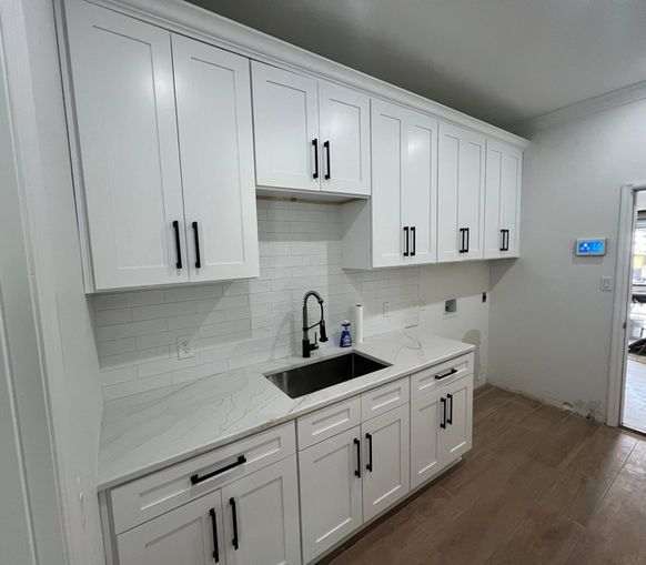 White kitchen cabinets with black hardware and a dark sink.