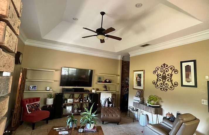 Living room with tan walls, recessed ceiling, TV, shelves, and various furniture.