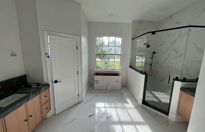Bright bathroom with white walls, window, glass shower, wooden vanity, and marble tile flooring.