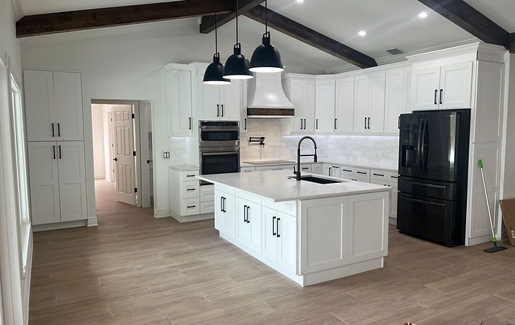 Modern white kitchen with black appliances, island, and overhead lights.