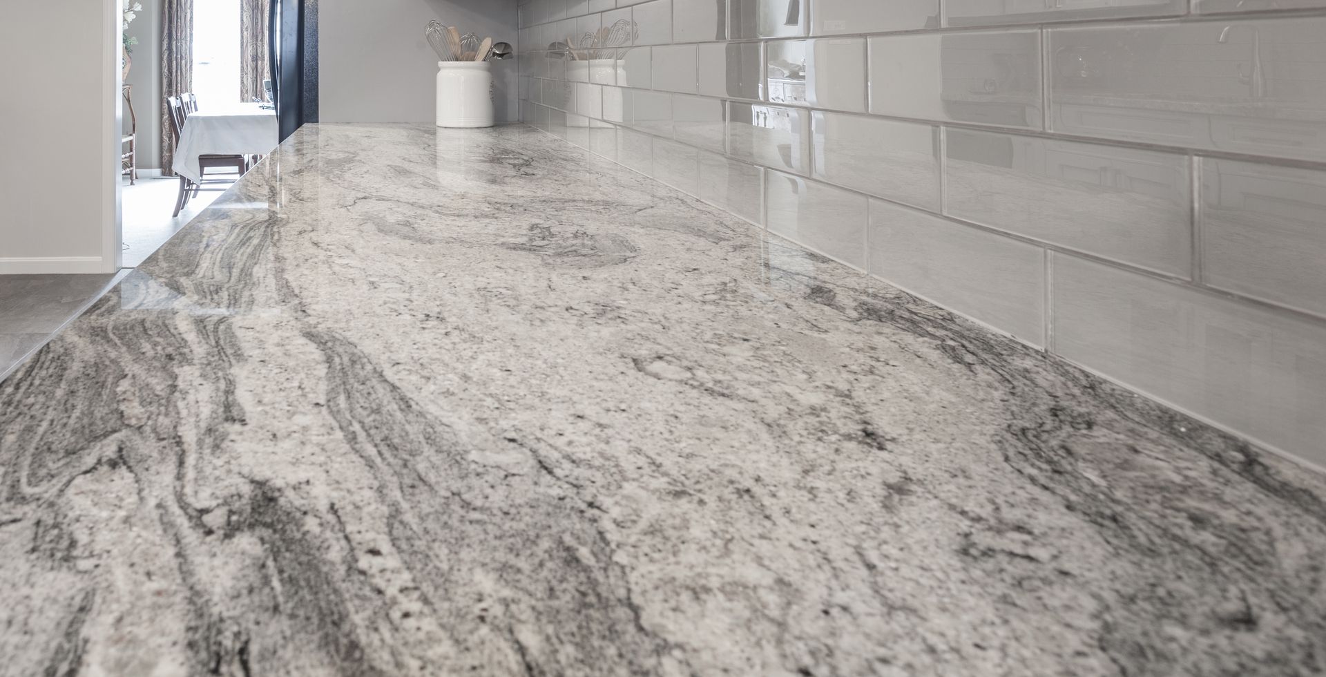 Close-up of a kitchen countertop made of swirling gray and white granite with gray tile backsplash.