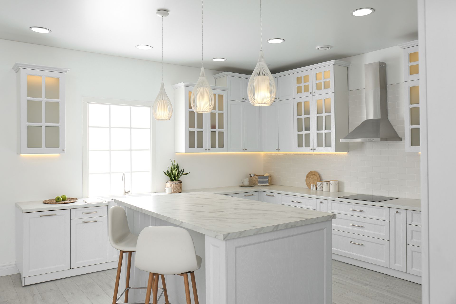 White kitchen with island, cabinets, pendant lights, and window; bright and modern.
