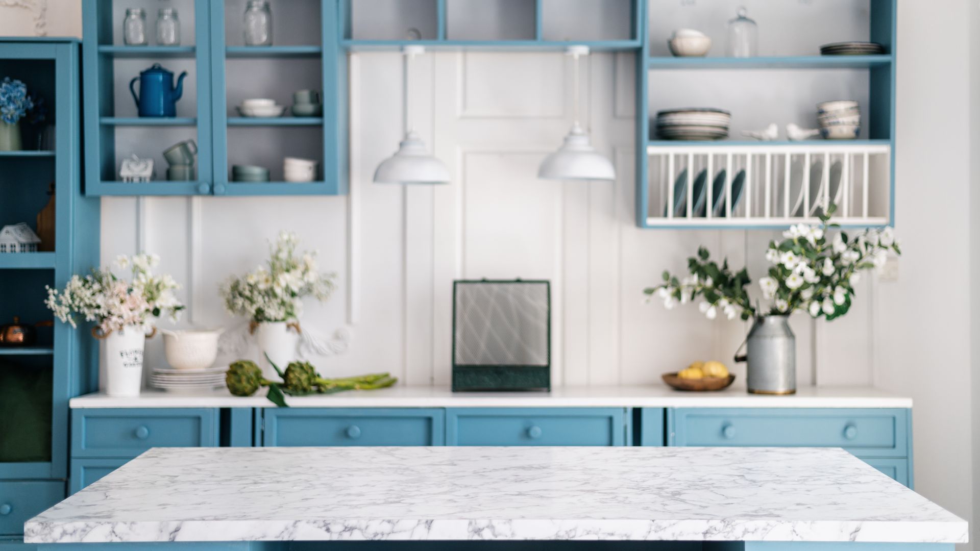 Blue and white kitchen with overhead cabinets, countertop with flowers, and pendant lights.