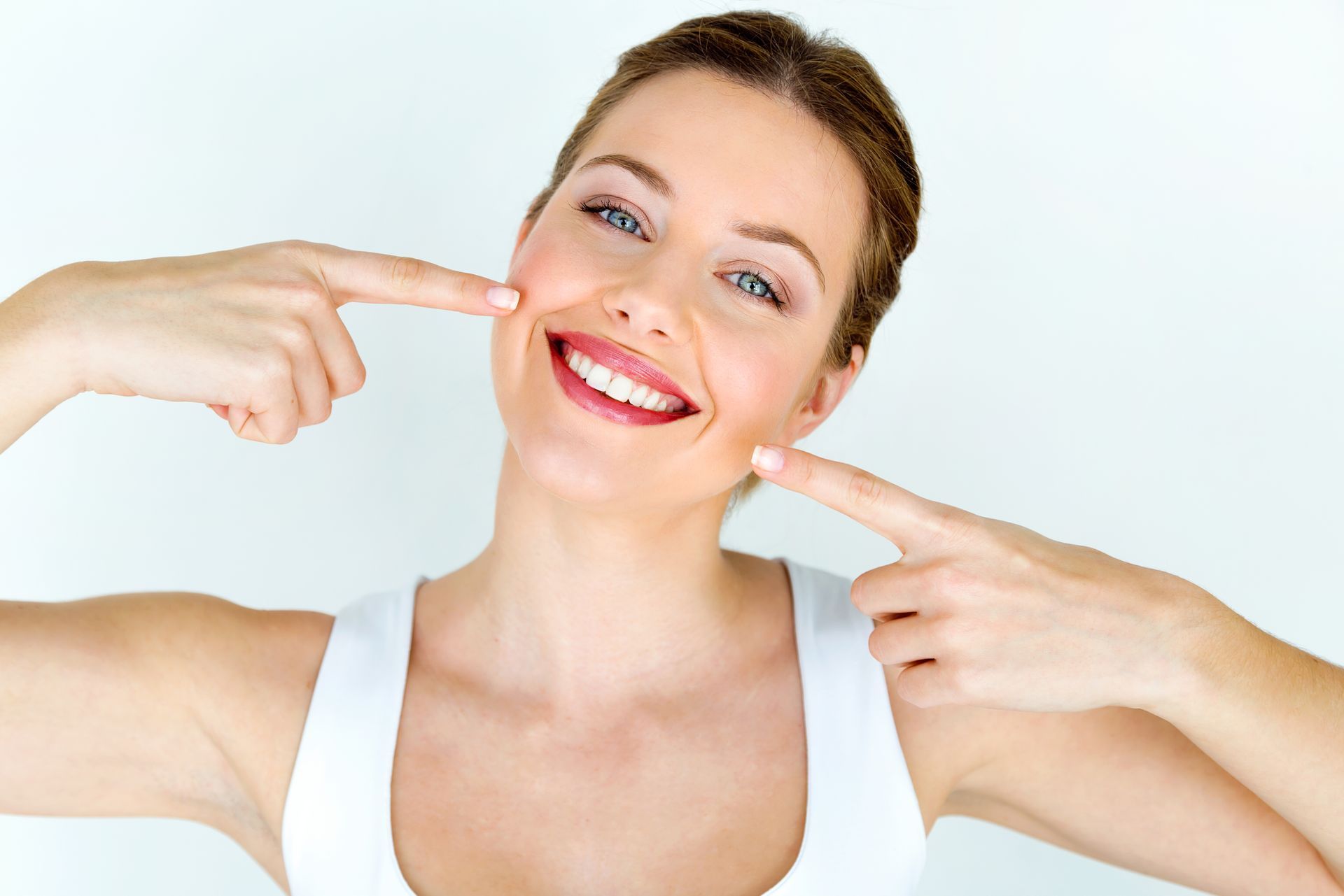 a woman is smiling and pointing at her teeth .