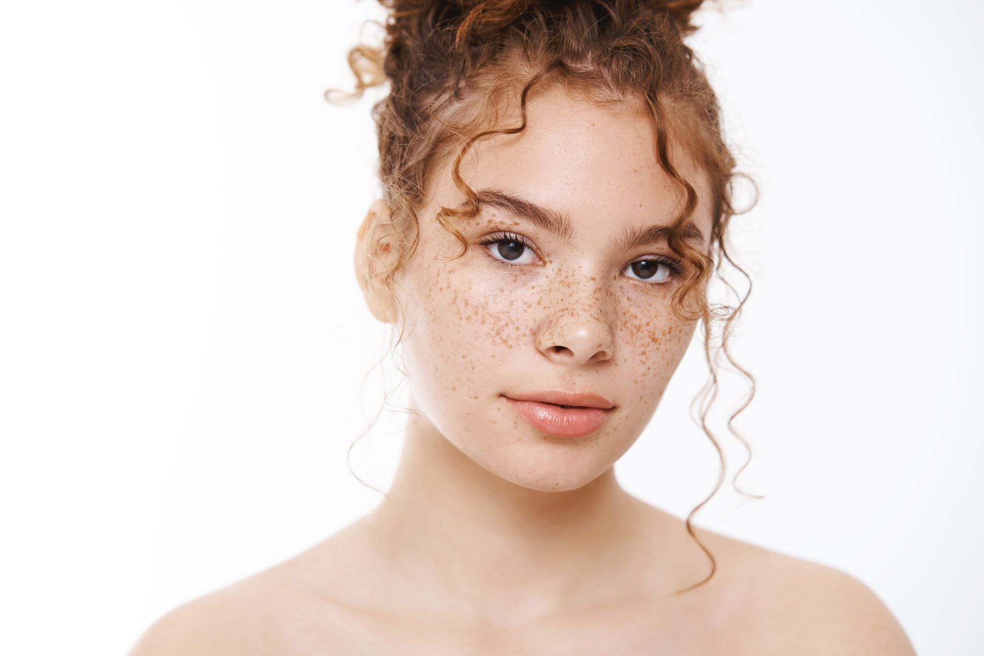 A young woman with curly hair and freckles is looking at the camera.