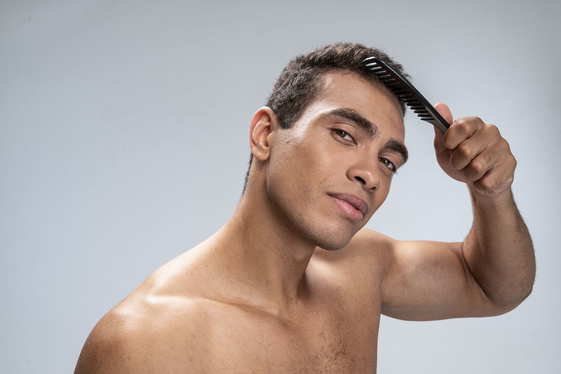 a shirtless man is brushing his hair with a comb .