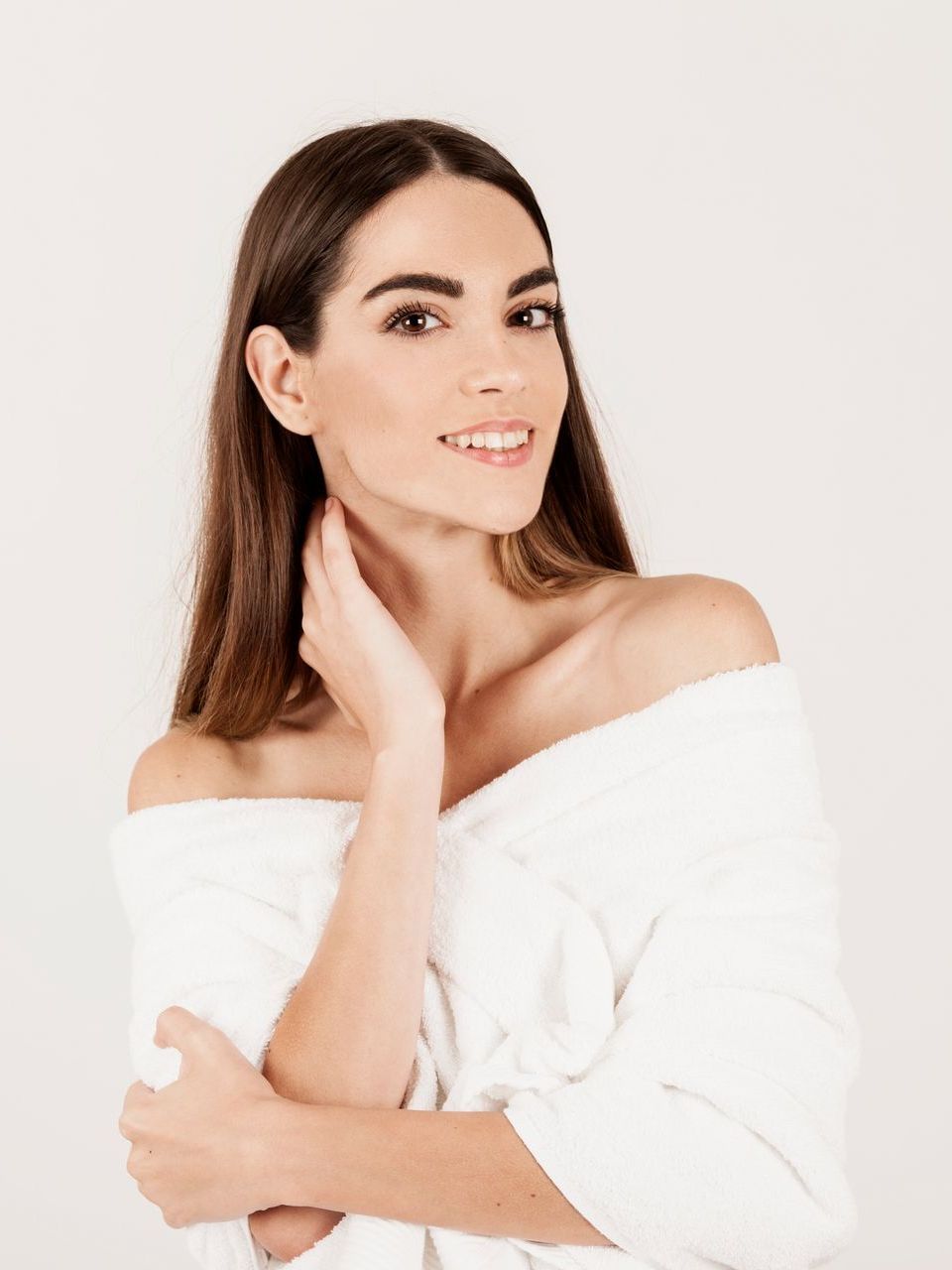 A woman is wearing a white off the shoulder sweater and smiling.