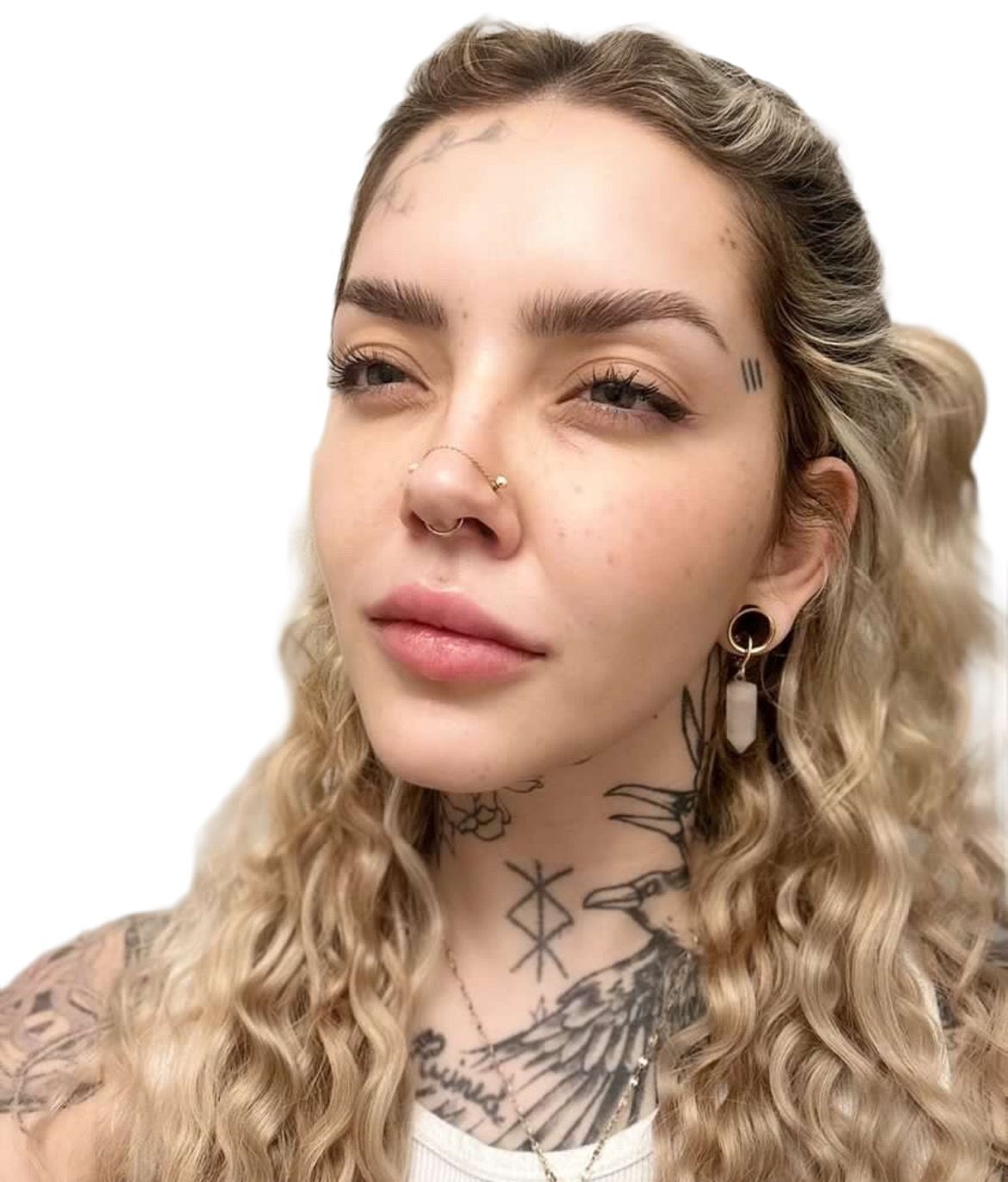 A woman with tattoos on her face and neck is wearing earrings and a nose ring.