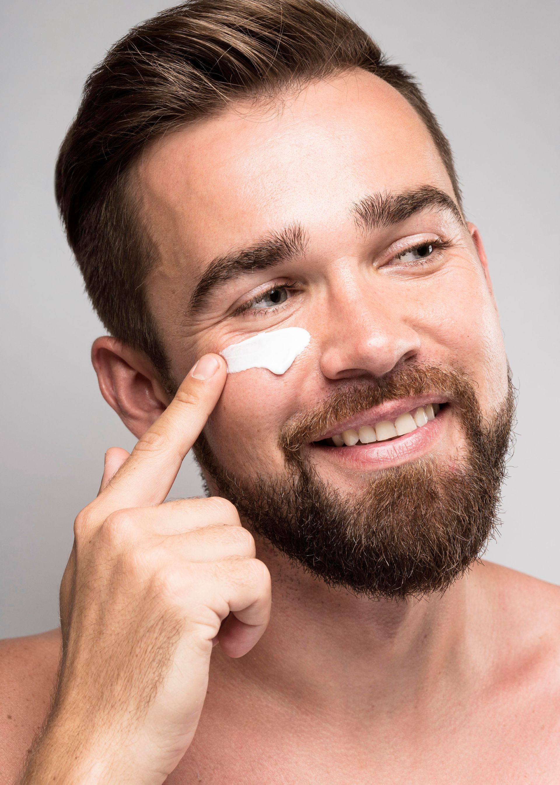 a man with a beard is applying cream to his face .