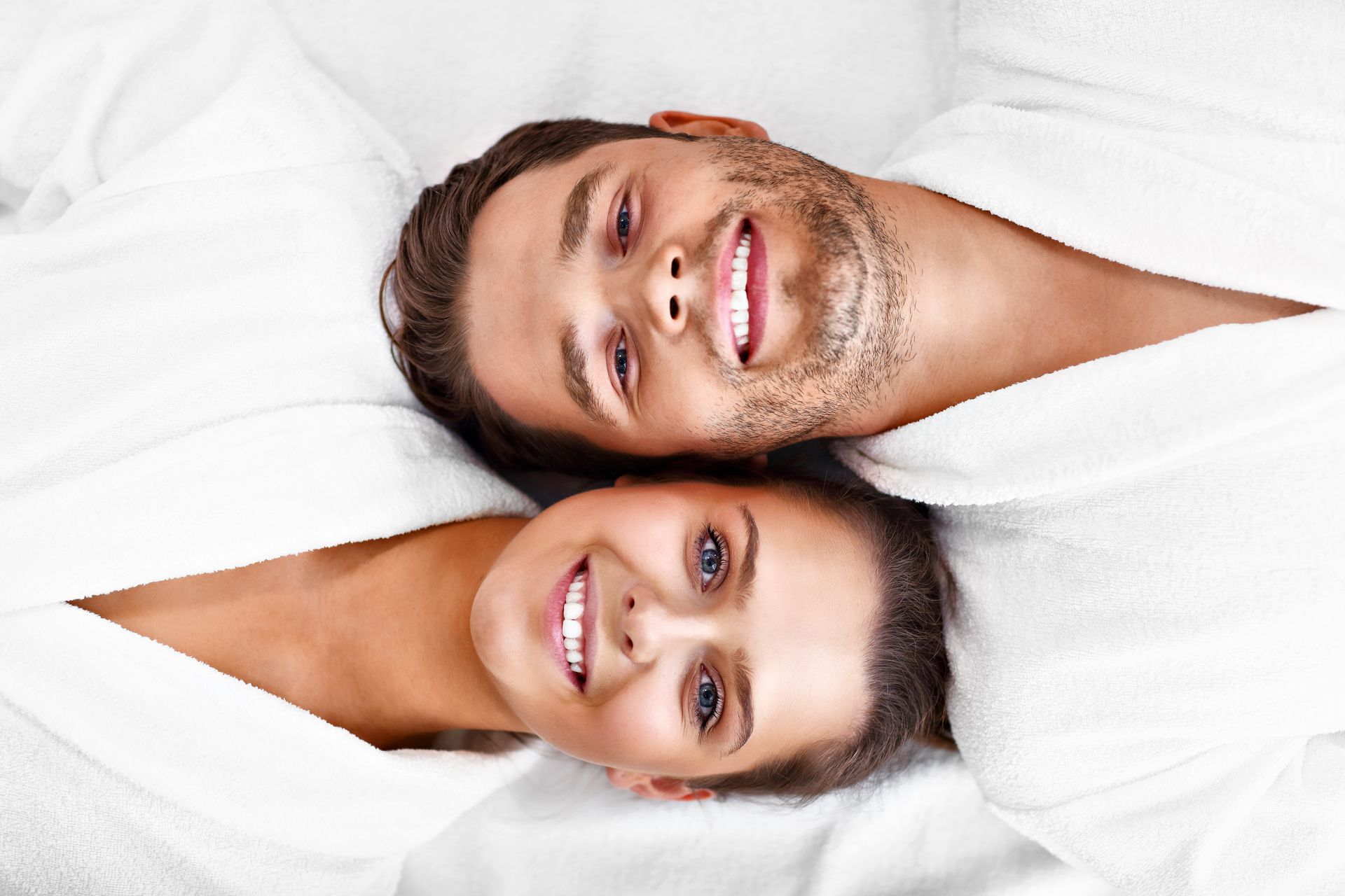 a man and a woman are laying next to each other on a bed and smiling .