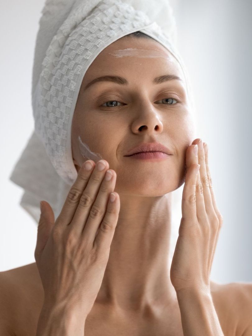 a woman with a towel wrapped around her head is applying lotion to her face .
