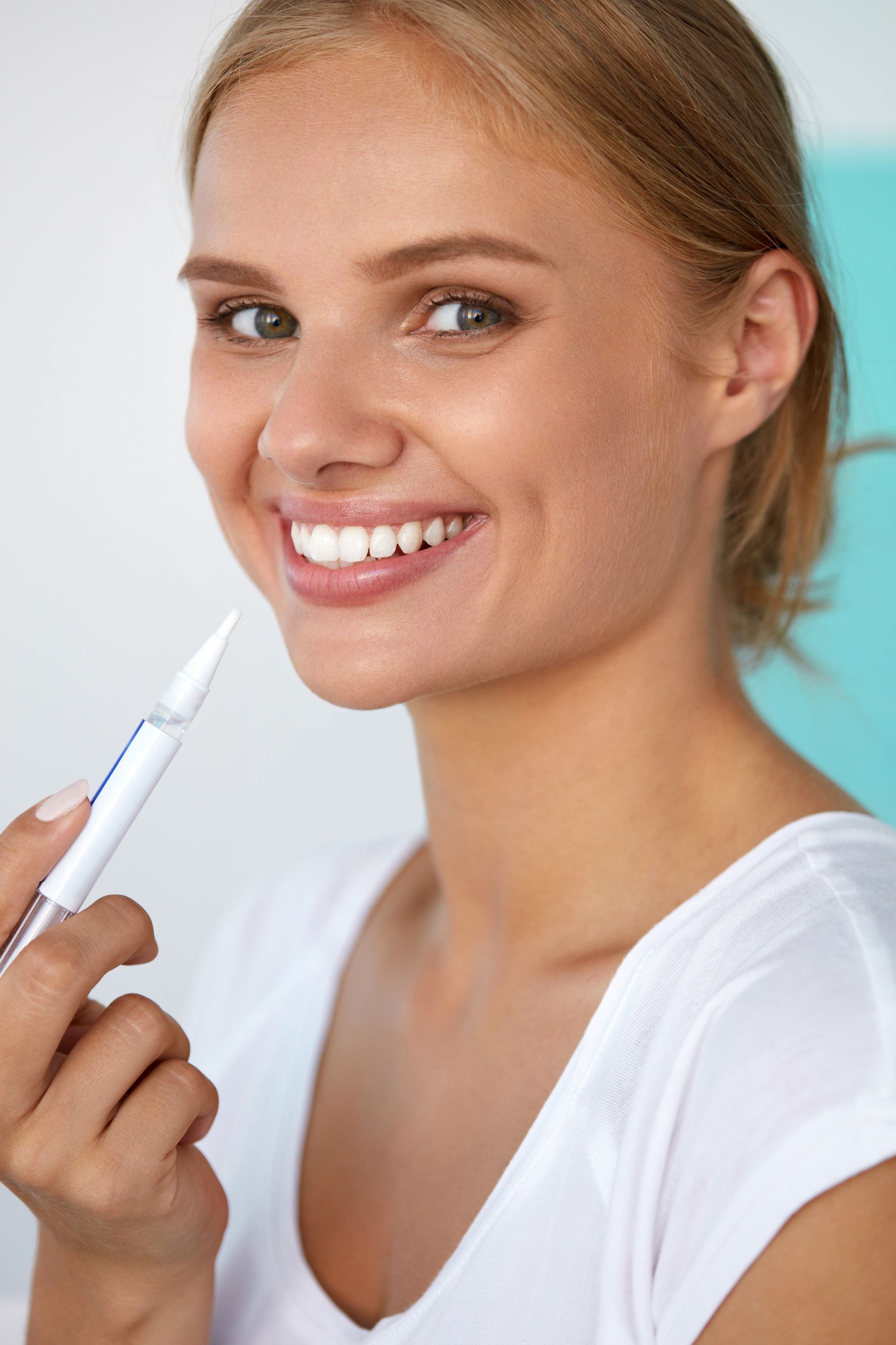 a woman is smiling while holding a whitening pen in her hand .