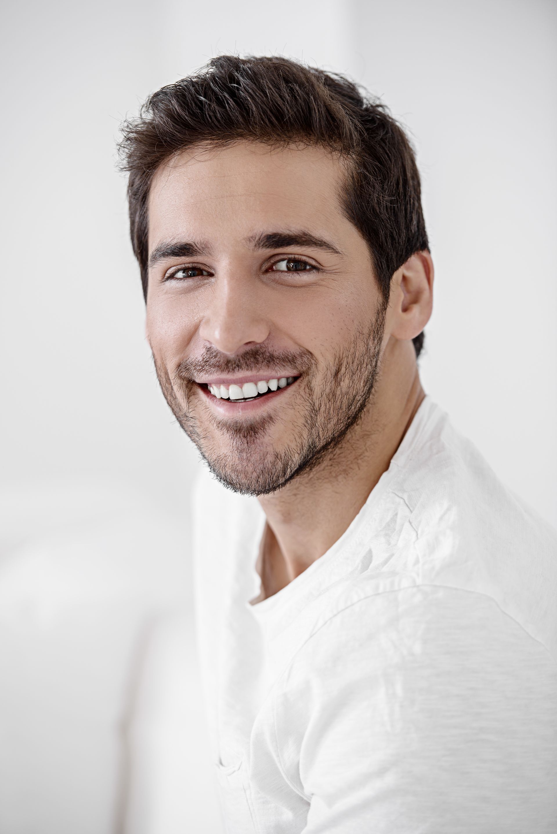 a man with a beard is smiling for the camera while wearing a white shirt .