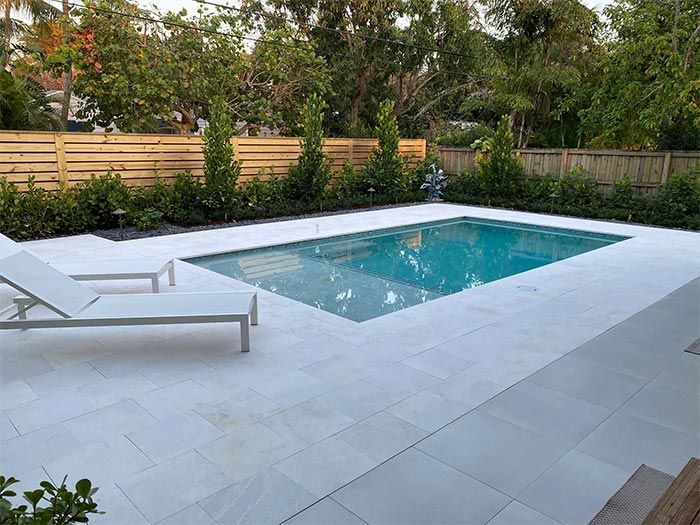 A large swimming pool is surrounded by lawn chairs and a wooden fence.