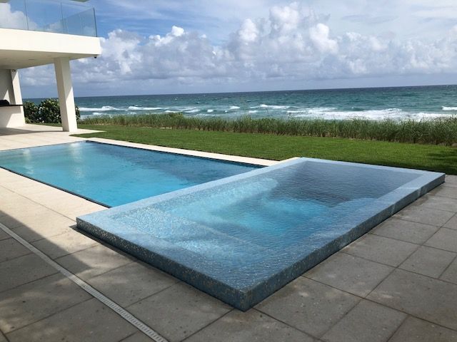 A large swimming pool with a hot tub next to it and a view of the ocean.