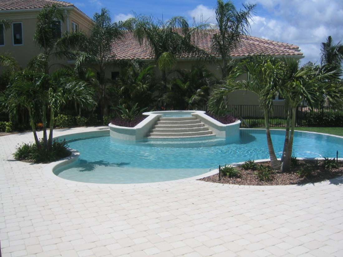 A large swimming pool surrounded by palm trees in front of a house