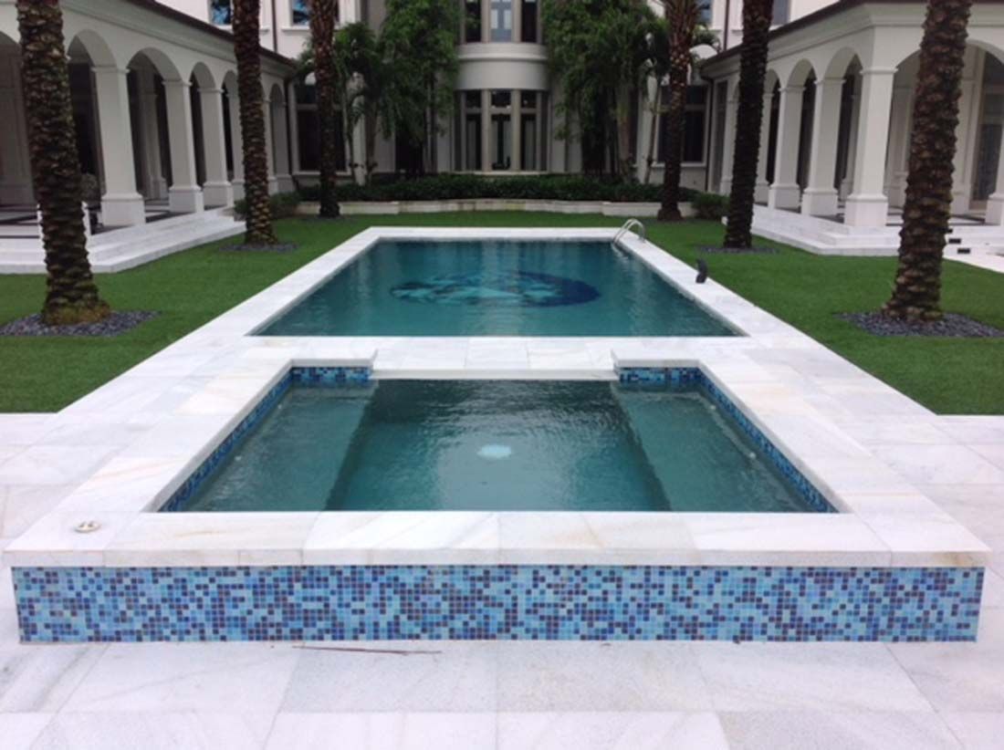 A large swimming pool is surrounded by a lush green lawn and palm trees.