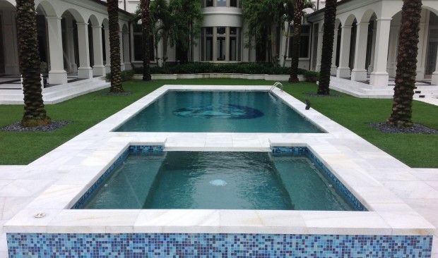 A large swimming pool is surrounded by palm trees and a lush green lawn.