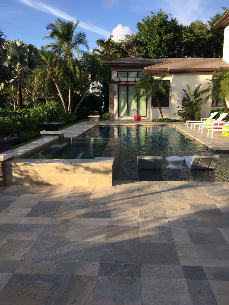 A large swimming pool is in front of a house surrounded by palm trees.